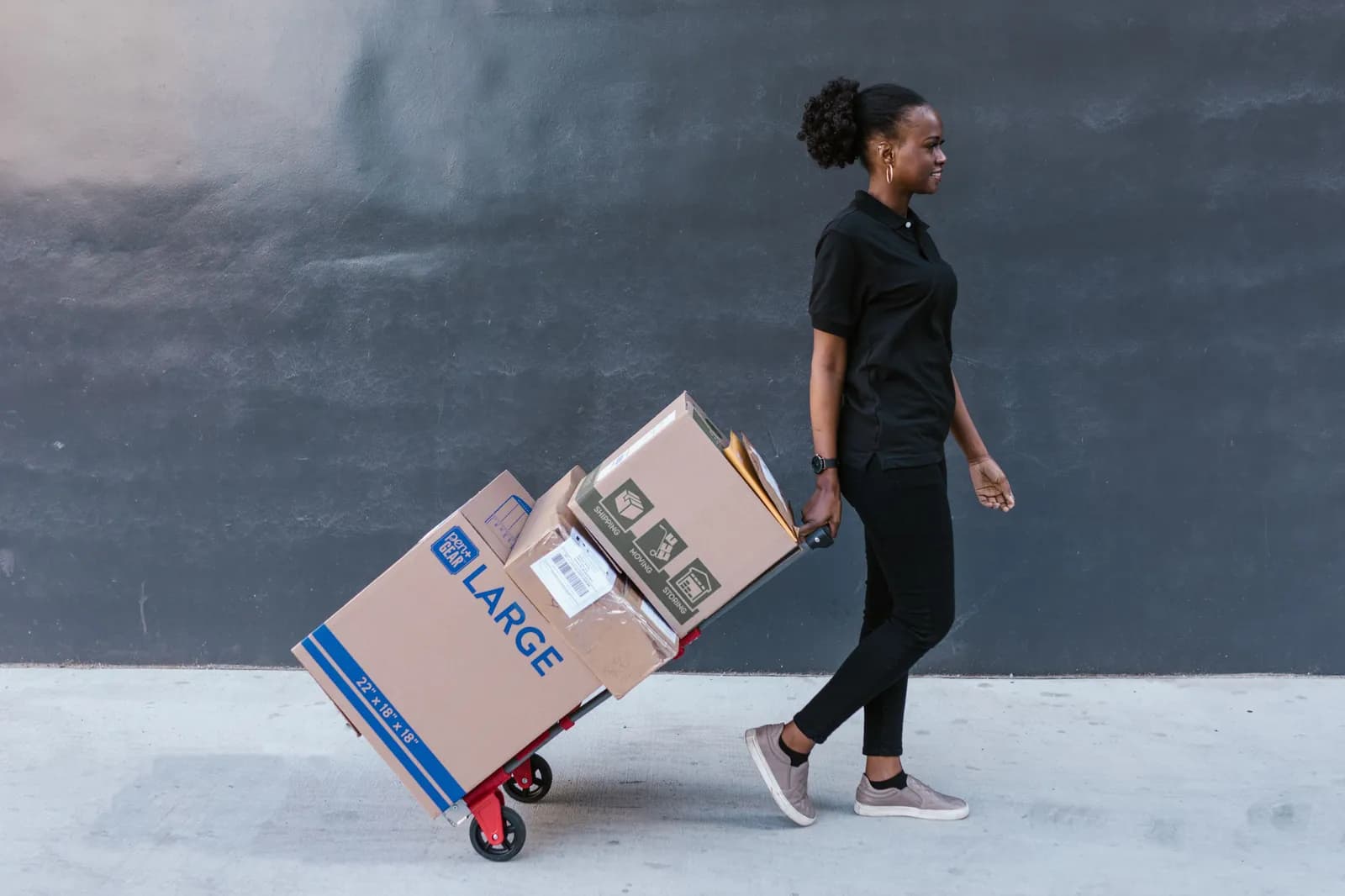Une femme tire un diable chargé de cartons prêts à partir.